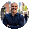 Smiling man in a dark button-down shirt standing on a city street.